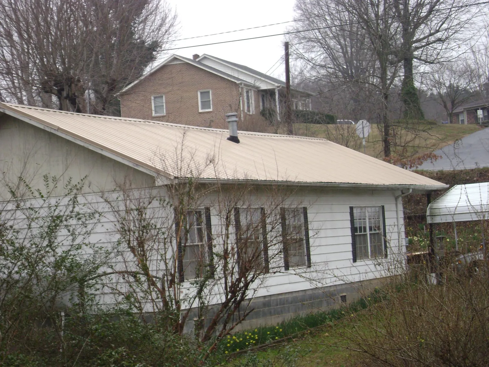 Tan metal roof on a white sided house set into a hillside — Commercial Roofing by Roofing Brothers in Dalton